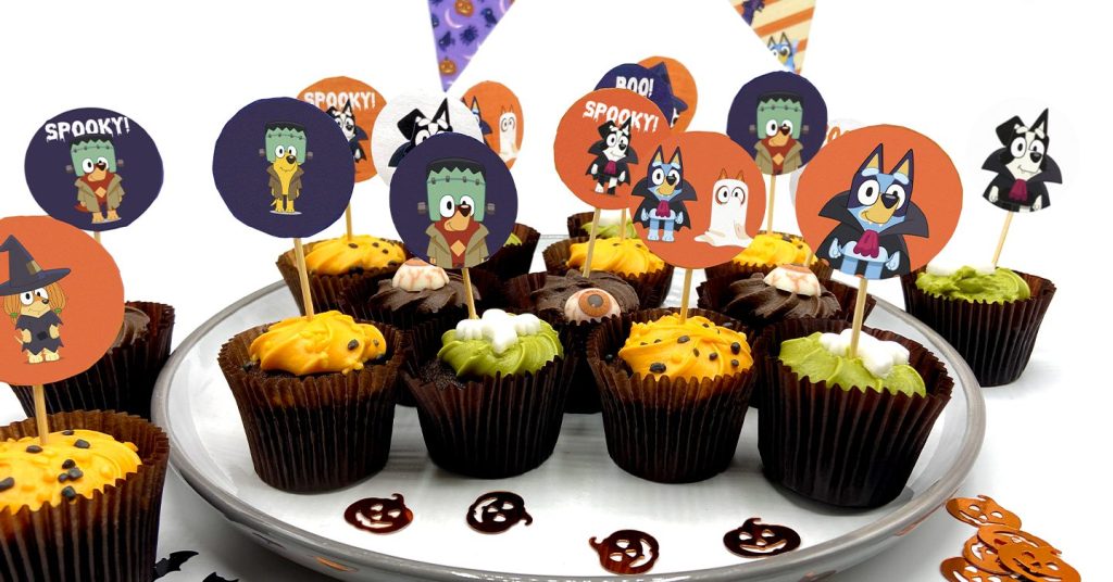 An image of orange, green and chocolate brown Halloween-themed cupcakes decorated with the spooky Bluey character cake toppers.